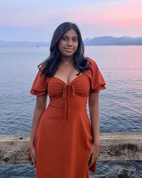 Pratiksha smiles while standing in front of water at sunset